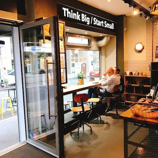 Blick durch die offene Tür auf die Fensterbank mit Gästen, darüber der Schriftzug Think Big Start Small