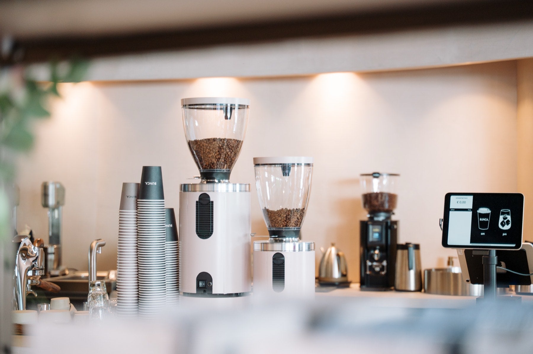 Zwei Kaffeemühlen, gestapelte Becher und das Kassendisplay auf dem Tresen